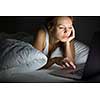 Pretty, young woman using her laptop computer in bed (color toned image; shallow DOF)