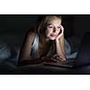 Pretty, young woman using her laptop computer in bed (color toned image; shallow DOF)