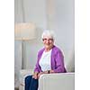 Portrait of a senior woman at home - Looking happy, looking at the camera, smiling while sitting on the sofa in her living room