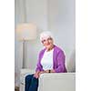 Portrait of a senior woman at home - Looking happy, looking at the camera, smiling while sitting on the sofa in her living room