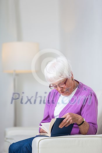 Portrait of a senior woman at home - Looking happy, looking at the camera, smiling while sitting on the sofa in her living room and reading a good book Portrait of a senior woman at home - Looking happy, looking at the camera, smiling while sitting on the sofa in her living room and reading a good book