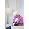 Portrait of a senior woman at home - Looking happy, looking at the camera, smiling while sitting on the sofa in her living room and reading a good book