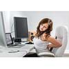 Young woman sitting at her computer desk suffering from acute back pain from her unhealthy sedentary lifestyle