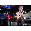 Pretty, young female commuter waiting for her daily train in a modern trainstation, using her cellphone while waiting (color toned image)