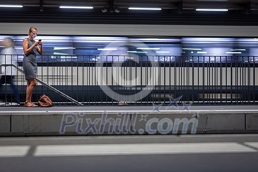 Pretty, young female commuter waiting for her daily train in a modern trainstation, using her cellphone while waiting (color toned image) Pretty, young female commuter waiting for her daily train in a modern trainstation, using her cellphone while waiting (color toned image)