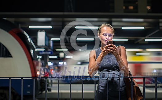 Pretty, young female commuter waiting for her daily train in a modern trainstation, using her cellphone while waiting (color toned image) Pretty, young female commuter waiting for her daily train in a modern trainstation, using her cellphone while waiting (color toned image)