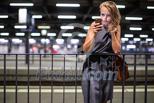 Pretty, young female commuter waiting for her daily train in a modern trainstation, using her cellphone while waiting (color toned image) Pretty, young female commuter waiting for her daily train in a modern trainstation, using her cellphone while waiting (color toned image)