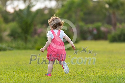 playful cute little girl cheerfully spending time while running in the spacious backyard on the grass