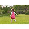 playful cute little girl cheerfully spending time while running in the spacious backyard on the grass