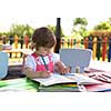 cute little girl cheerfully spending time using pencil crayons while drawing a colorful pictures in the outside playschool
