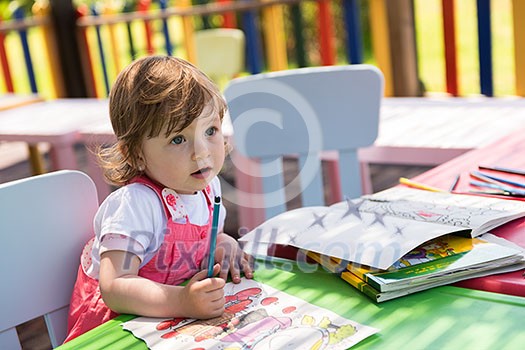 cute little girl cheerfully spending time using pencil crayons while drawing a colorful pictures in the outside playschool cute little girl cheerfully spending time using pencil crayons while drawing a colorful pictures in the outside playschool