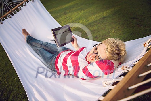 young woman using a tablet computer while relaxing on hammock in a peaceful garden during holiday young woman using a tablet computer while relaxing on hammock in a peaceful garden during holiday