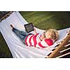 young woman using a tablet computer while relaxing on hammock in a peaceful garden during holiday