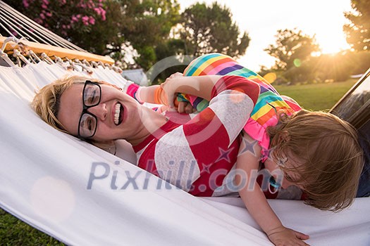 Happy mother and her little daughter enjoying free time using tablet computer while relaxing in a hammock during sunny day on holiday home garden Happy mother and her little daughter enjoying free time using tablet computer while relaxing in a hammock during sunny day on holiday home garden