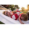 Happy mother and her little daughter enjoying free time using tablet computer while relaxing in a hammock during sunny day on holiday home garden