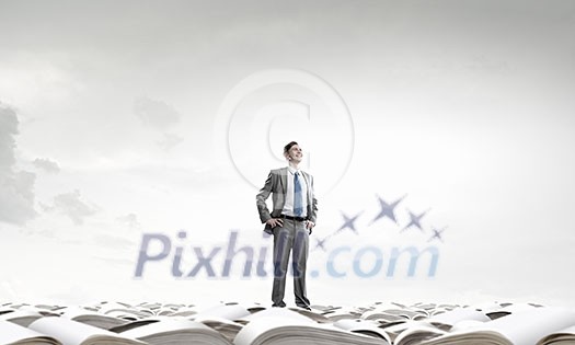 Young confident businessman with arms on waist standing on pile of old books Young confident businessman with arms on waist standing on pile of old books