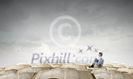 Young businessman sitting alone on pile of old books Young businessman sitting alone on pile of old books