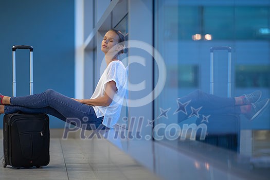 Exhausted female passenger waiting for her re-scheduled/delayed flight with her luggage at an international airport Exhausted female passenger waiting for her re-scheduled/delayed flight with her luggage at an international airport