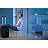 Exhausted female passenger waiting for her re-scheduled/delayed flight with her luggage at an international airport