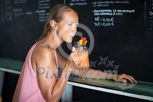 Pretty, young woman enjoying a refreshing drink in a bar on a hot summer day Pretty, young woman enjoying a refreshing drink in a bar on a hot summer day
