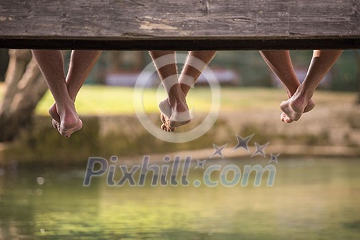 group of people sitting at wooden bridge over the river with a focus on hanging legs group of people sitting at wooden bridge over the river with a focus on hanging legs
