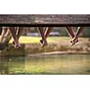 group of  people sitting at wooden bridge over the river with a focus on hanging legs