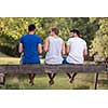 group of young men enjoying watermelon while sitting on the wooden bridge over the river in beautiful nature