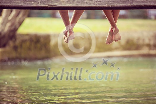 group of people sitting at wooden bridge over the river with a focus on hanging legs group of people sitting at wooden bridge over the river with a focus on hanging legs