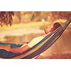 Young man resting on hammock while enjoying nature on the river bank