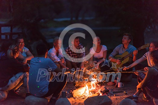 a group of happy young friends relaxing and enjoying summer evening around campfire on the river bank a group of happy young friends relaxing and enjoying summer evening around campfire on the river bank