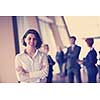 Smilling young business woman in front her team blured in background. Group of young business people. Modern bright  startup office interior.