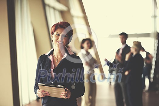 Smilling young business woman with tablet computer in front her team blured in background. Group of young business people. Modern bright startup office interior. Smilling young business woman with tablet computer in front her team blured in background. Group of young business people. Modern bright startup office interior.