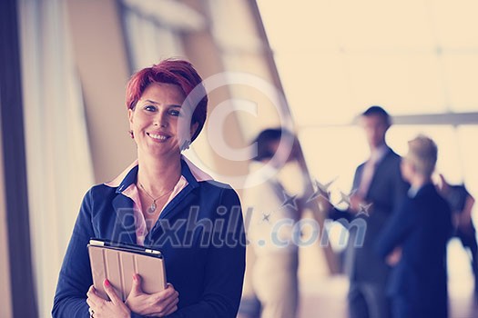 Smilling young business woman with tablet computer in front her team blured in background. Group of young business people. Modern bright startup office interior. Smilling young business woman with tablet computer in front her team blured in background. Group of young business people. Modern bright startup office interior.