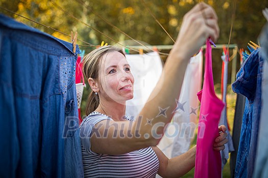 Young woman putting laundry on a rope in her garden, taking great care of her family on a daily basis Young woman putting laundry on a rope in her garden, taking great care of her family on a daily basis