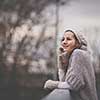 Autumn/winter portrait: young woman dressed in a warm woolen cardigan posing outside in a city park