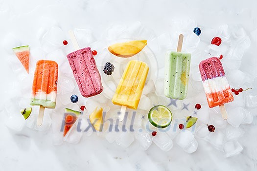 Collection of colorful bright natural ice cream popsicles with fruit and berries on ice cubes. Homemade healthy ice lolly. Flat lay