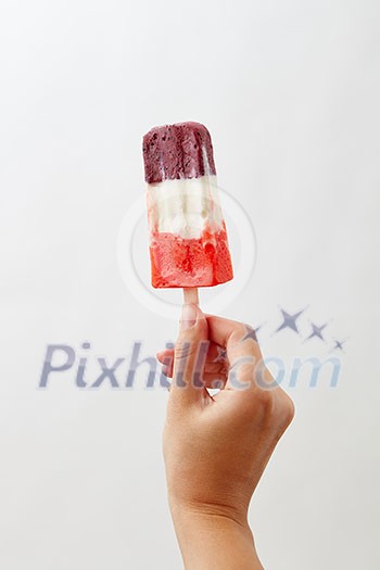 A woman's hand holds a colored berry ice cream lolly on a white background with copy space. Healthy food. Business concept concept A woman's hand holds a colored berry ice cream lolly on a white background with copy space. Healthy food. Business concept concept