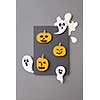 Gray frame of flying ghosts, spirits and yellow scary pumpkins, handcraft from paper on a gray background with copy space. Halloween concept. Flat lay.
