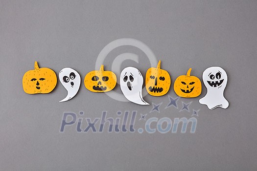 Colorful Halloween handcraft composition with flying floating ghost spirit and smiling yellow pumpkins on a gray paper background, place for text. Flat lay. Colorful Halloween handcraft composition with flying floating ghost spirit and smiling yellow pumpkins on a gray paper background, place for text. Flat lay.