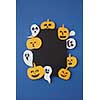 Greeting decorative card handcraft with paper horrible smiling spirits and ghosts and laughing pumpkin on a blue paper background, place under text. Top view.
