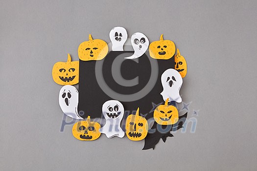 Square creative frame of black paper with handcraft laughing flying ghosts, spirits, scary pumpkins, black bats on a gray background, place for text. Square creative frame of black paper with handcraft laughing flying ghosts, spirits, scary pumpkins, black bats on a gray background, place for text.