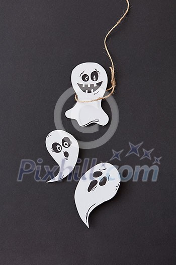 Halloween greeting card with laughing flying scary ghost hanging from a rope handmade from paper on a black background, copy space. Flat lay Halloween greeting card with laughing flying scary ghost hanging from a rope handmade from paper on a black background, copy space. Flat lay