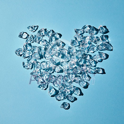 A pattern of transparent ice cubes in the shape of a heart on a blue paper background with copy space. As a background for a postcard. Flat lay A pattern of transparent ice cubes in the shape of a heart on a blue paper background with copy space. As a background for a postcard. Flat lay