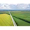 Aerial view of road through beautiful green field in the evening in summer. Beautiful landscape with speedway trees, green agricultural fields. Top view from flying drone.
