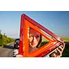 Pretty, young woman setting the safety triangle on the roadside after her car has broken down