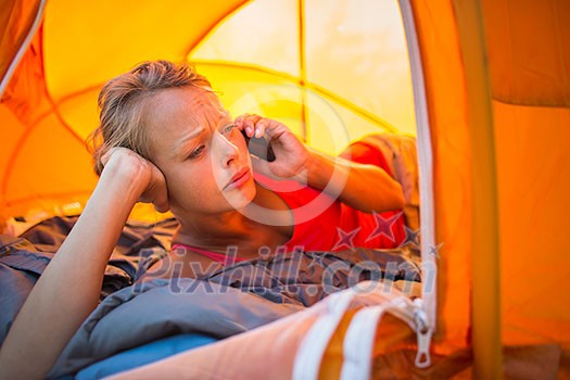 Pretty, young woman camping outdoors, lying in the tent in the morning, using her smart phone Pretty, young woman camping outdoors, lying in the tent in the morning, using her smart phone
