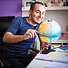 Handsome college student studing at home for his geography exam using a globus