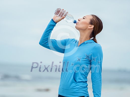 Sporty young woman drinking water on the sea coast Sporty young woman drinking water on the sea coast
