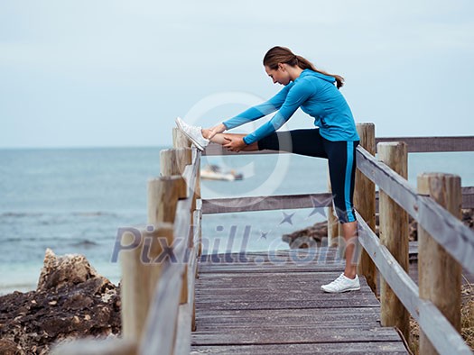 Sporty young woman stretching next to the sea coast Sporty young woman stretching next to the sea coast