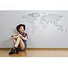 Smiling young beautiful woman sitting on the floor against a wall with world map sketch. Mixed media